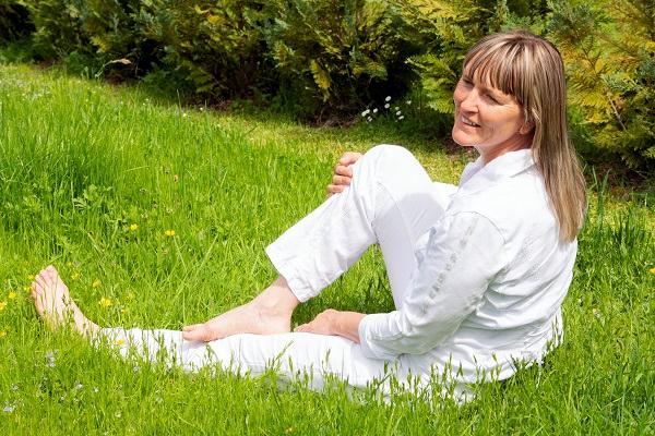 Eine Frau sitzt mit nackten Füßen im Gras und lcht den Betrachter an.